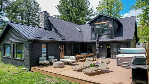 Une cabane en rondins moderne dotée d’une terrasse, d’un espace salon extérieur et d’un barbecue.