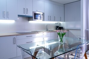 Une cuisine moderne avec des meubles blancs, une table à manger en verre et une machine à café.
