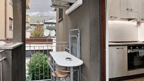 Ein Balkon mit Tisch und Stuhl, Blick auf Gebäude sowie eine Küchenzeile mit Schränken und Backofen.