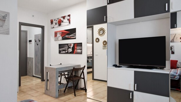 Ein modernes Wohnzimmer mit Fernseher, Esstisch, Stühlen und einer Küchenzeile mit Schränken und einer Mikrowelle.