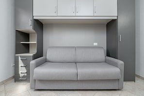 Een grijze bank in een kamer met grijze kasten en een klein rek.
