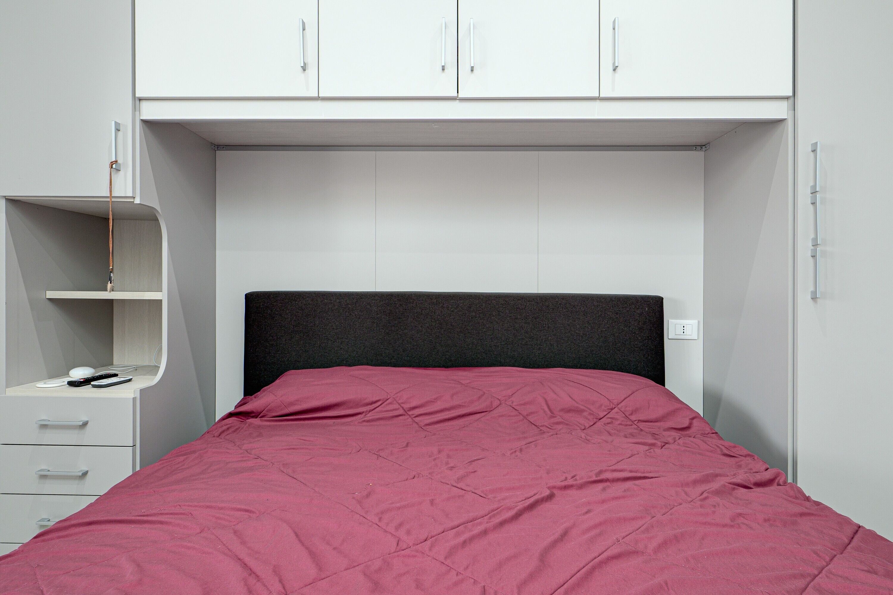 A bed with a red bedspread, a white dresser with drawers, and a white wardrobe with doors.