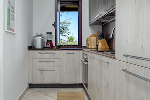 Een keuken met een raam, een broodrooster, een blender en een houten snijplank met messen.