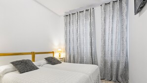 Un dormitorio con dos camas, cabeceros de madera, una lámpara de noche y cortinas estampadas.