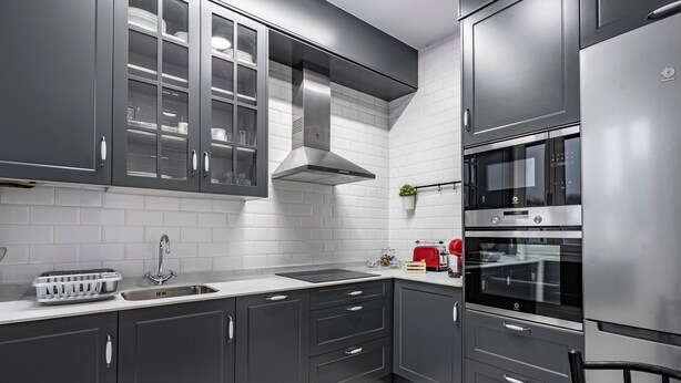 Una cocina moderna con armarios grises, una campana extractora de acero inoxidable, un horno empotrado y una mesa de comedor de vidrio.