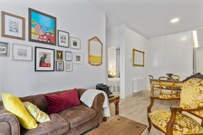 A living room with a brown sofa, yellow pillows, a coffee table, and a dining area with a wooden table and chairs.