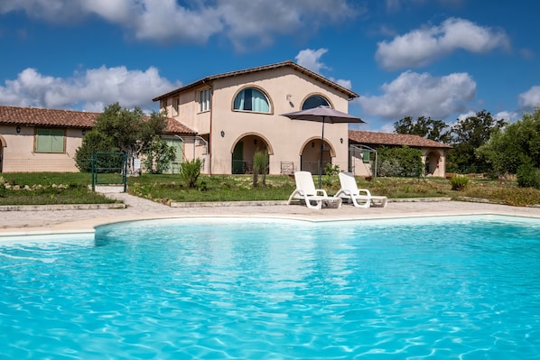 Une maison avec une piscine, deux chaises longues et une pergola.