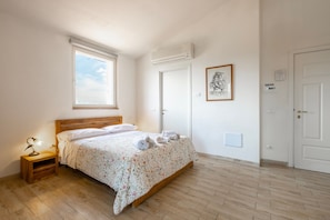 Une chambre à coucher avec un lit en bois, une table de chevet, une fenêtre, un climatiseur, un tableau encadré et une porte.