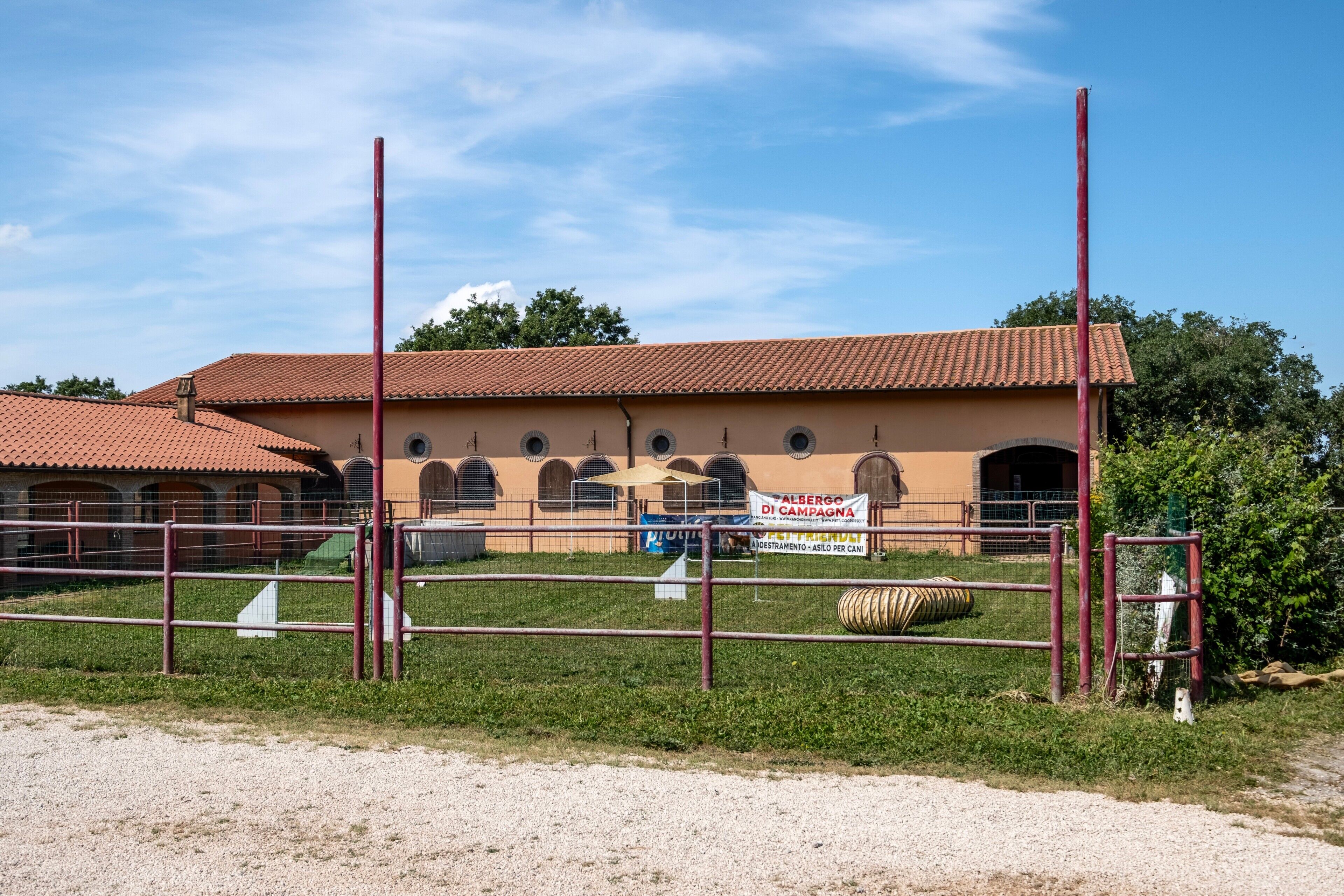 A building with a red-tiled roof, a fenced area with a gravel path, and a signboard.