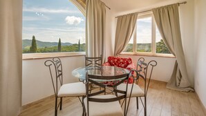 A dining area with a glass table and chairs, a red floral sofa, and a view of greenery and hills through large windows. - Apartment 'Erica' with Shared Pool, Wi-Fi and Air Conditioning (Manciano)