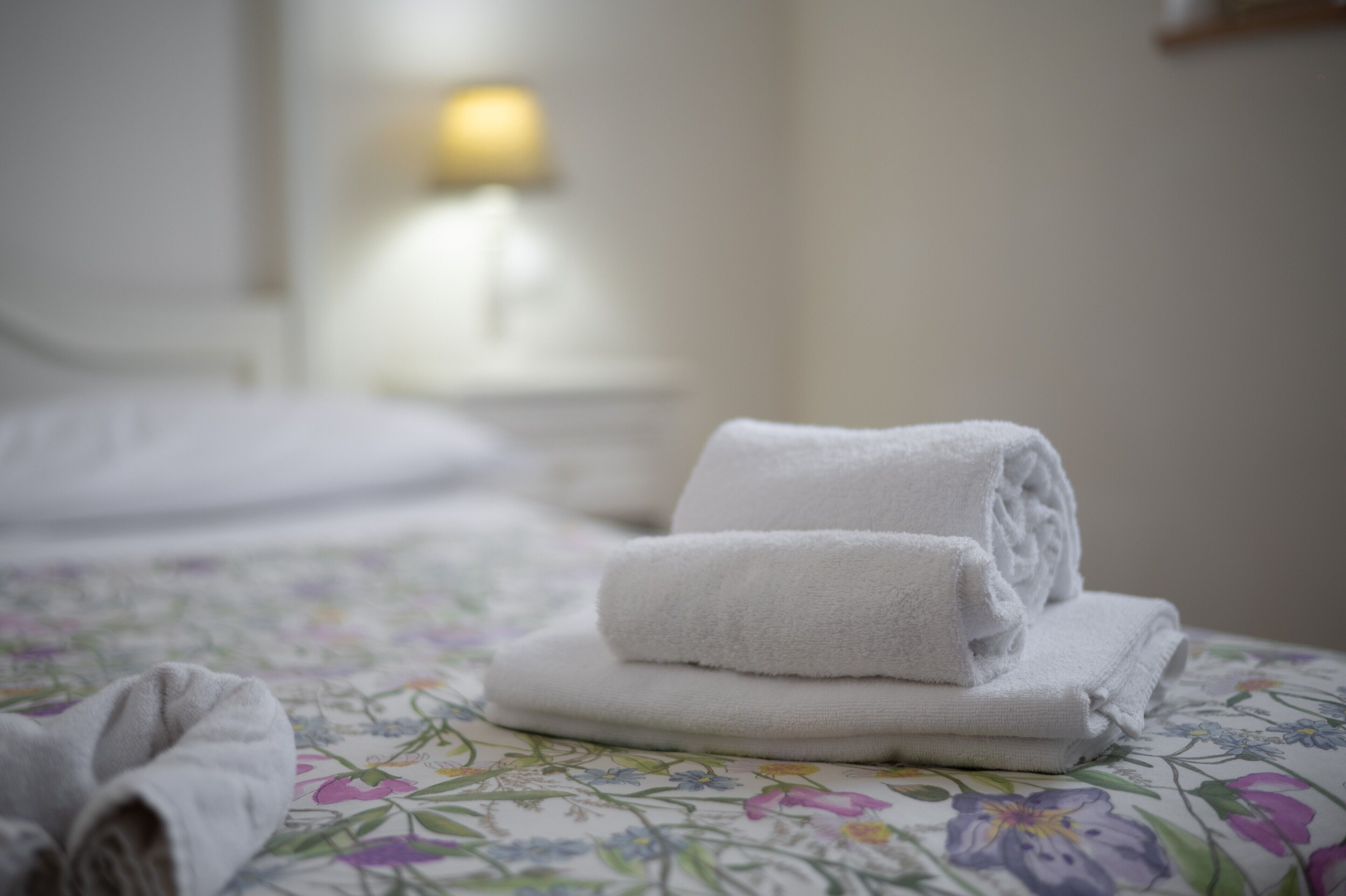 A neatly made bed with a floral-patterned bedspread and a stack of white towels.