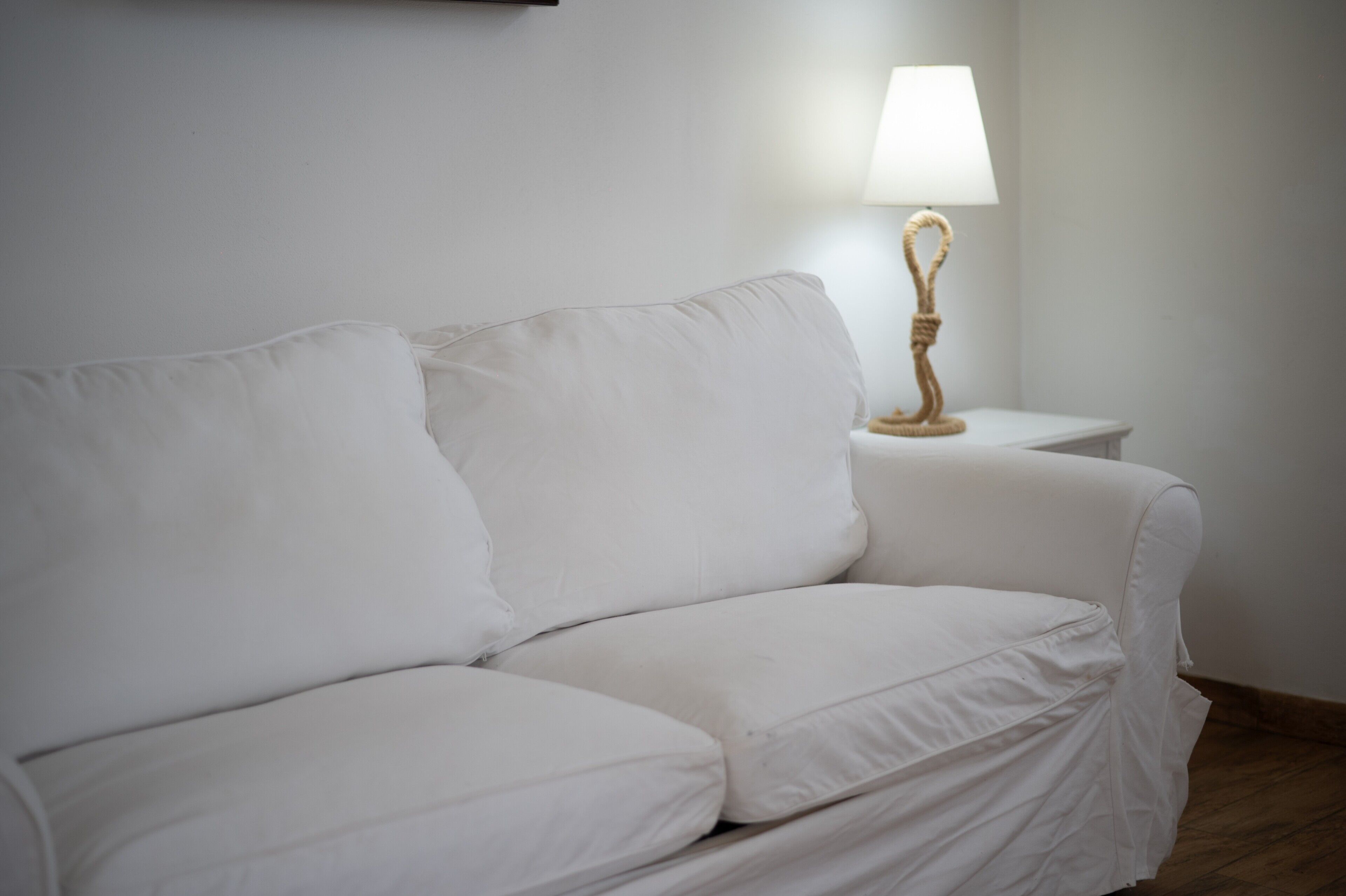 Ein weißes Sofa mit einer Lampe auf einem Beistelltisch in einem Raum mit schlichten Wänden.