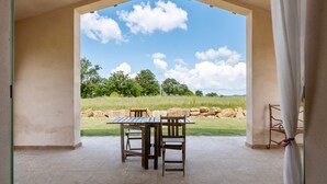Une terrasse extérieure avec une table et des chaises, une vue sur un champ verdoyant et un ciel dégagé.