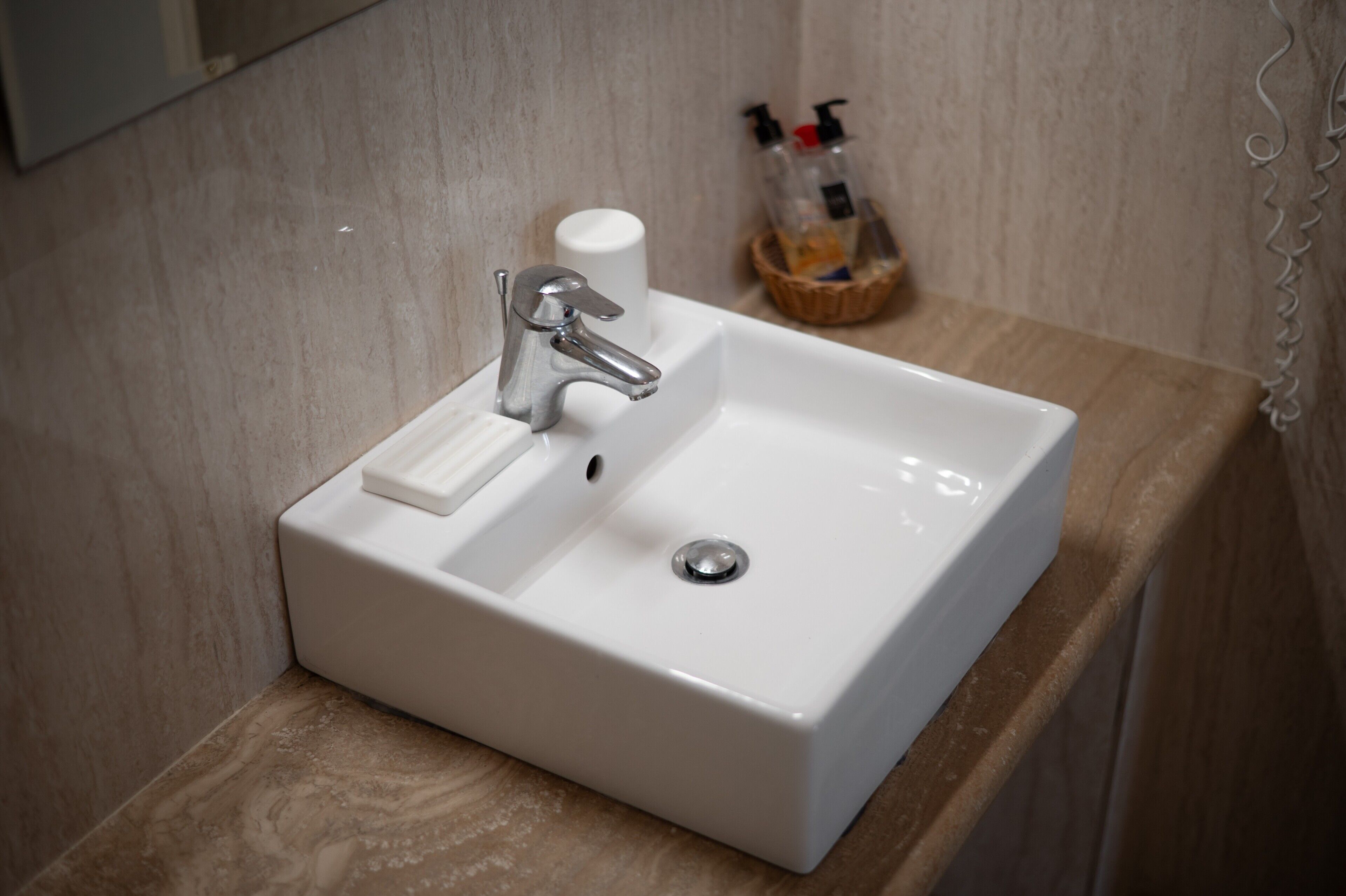 A bathroom with a white sink, a mirror, and a soap dispenser on the countertop.