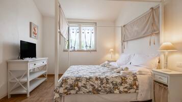 Ein Schlafzimmer mit Himmelbett, einem Fernseher auf einer weißen Kommode und einem Fenster mit Vorhängen.