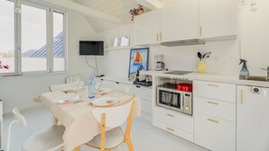 Una cocina moderna con armarios blancos, un comedor con mesa lista para dos personas y un ventanal con vistas a las montañas.