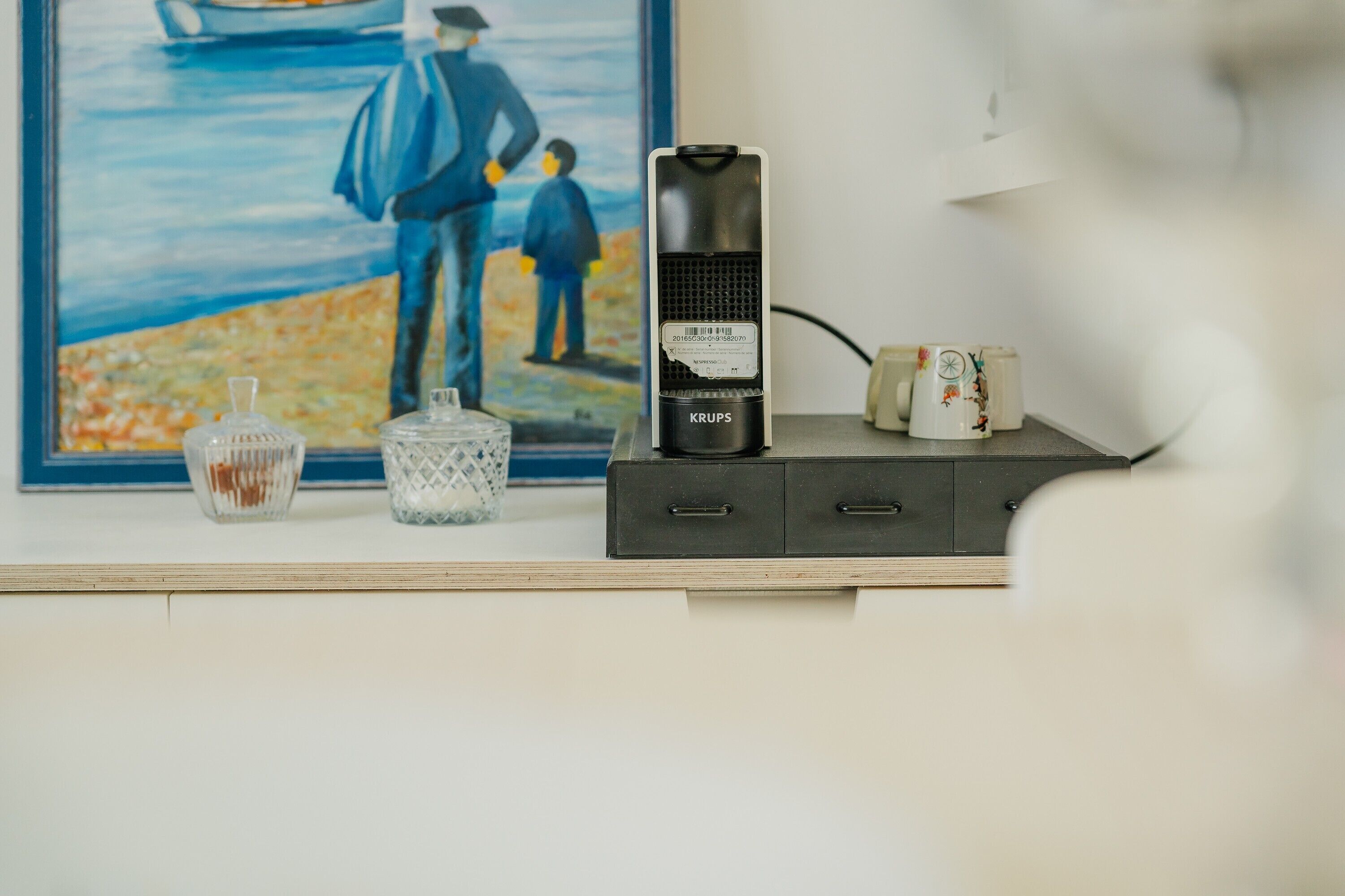 A desktop computer on a wooden shelf, a framed painting, and a coffee maker.