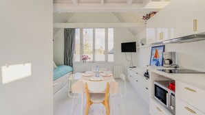 Una habitación compacta con cama, una mesa de comedor con sillas, una zona de cocina con microondas y un televisor instalado en la pared.