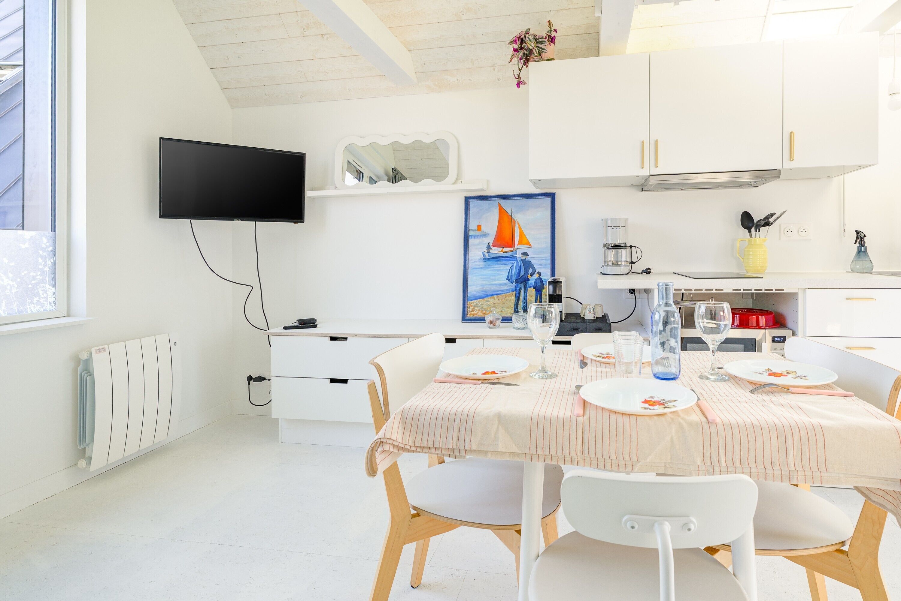 Cucina moderna con mobili bianchi, una televisione a schermo piatto e zona pranzo con tovaglia a righe.