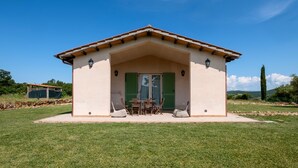 A building with a flat roof, a covered patio with a table and chairs, and a door with green shutters. - Room 'Timo' with Shared Pool, Wi-Fi and Air Conditioning (Manciano)