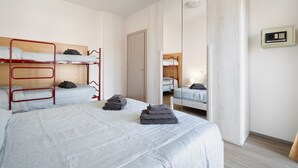 A dorm-style room with bunk beds, a mirror, a wardrobe, and a bedside table.