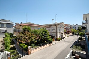 Une rue résidentielle bordée de maisons, avec un ciel dégagé et un trottoir ombragé par des arbres.