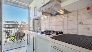 A modern kitchen with a gas stove, stainless steel range hood, and a view of the balcony.