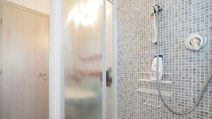 A bathroom with a glass door, a shower with a handheld showerhead, and a tiled wall.