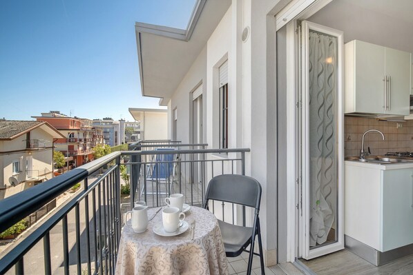 A balcony with a table set for two, a chair, and a kitchen with white cabinets and a tiled backsplash.