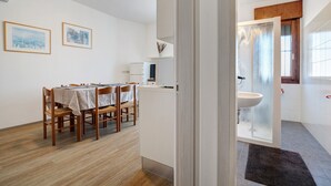 A room with a dining table, chairs, a cabinet, a bathroom with a sink, and a frosted glass door.