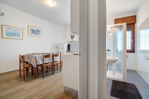 A room with a dining table, chairs, a cabinet, a bathroom with a sink, and a frosted glass door.