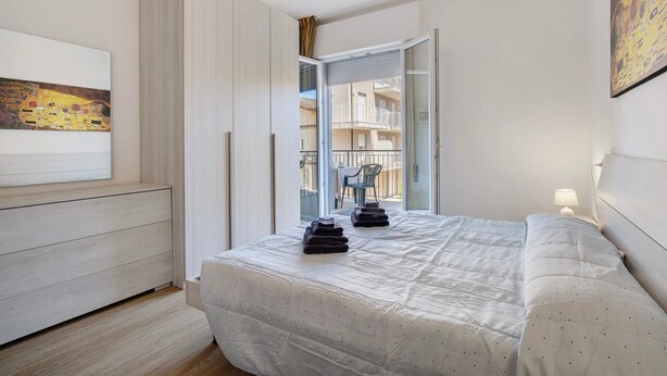 A bedroom with a bed, a wardrobe, a painting, and a balcony with a view of buildings. - Apartment '1 Piano' with Shared Terrace, Wi-Fi and Air Conditioning (Jesolo)