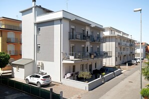 Un immeuble résidentiel à plusieurs étages, doté de balcons, avec une voiture garée devant et un lampadaire.