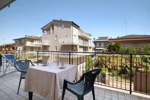 Un balcon avec une table et des chaises, une balustrade et une vue sur les bâtiments environnants.