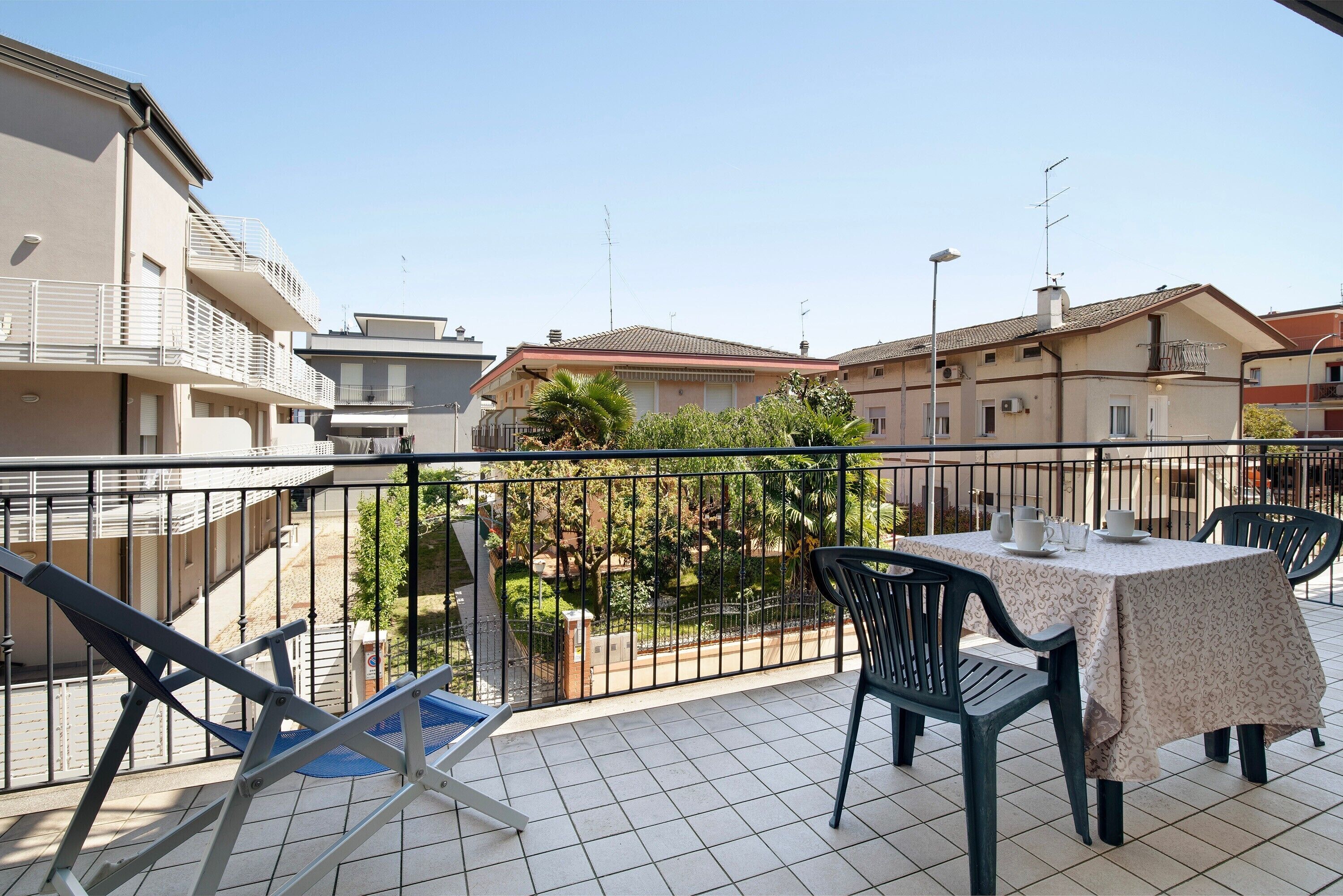 Ein Balkon mit Tisch und Stühlen, ein blauer Stuhl sowie Blick auf Gebäude und Grünflächen.