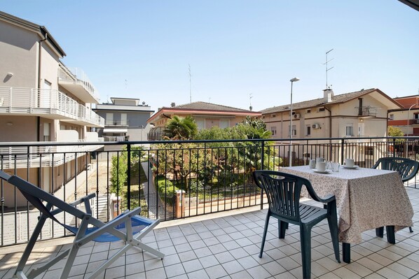 Un balcon avec une table et des chaises, une chaise bleue, et une vue sur des bâtiments et de la verdure.