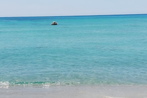 Een strand met helder turquoise water en een rotsformatie in de verte.