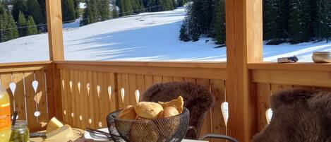 A wooden deck with a table set for breakfast, a chair, and a view of a snowy mountain landscape.