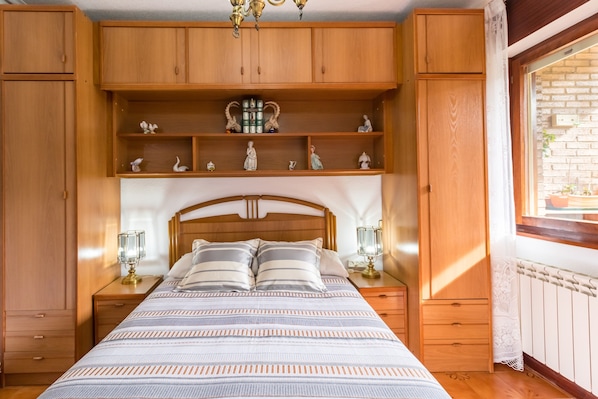 Une chambre à coucher avec une tête de lit en bois, un lit avec une literie à rayures, deux tables de chevet avec des lampes et des étagères en bois au-dessus du lit.