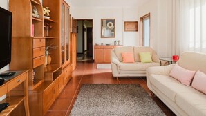 A living room with a sofa, TV, wooden cabinet, and a rug. - Room 'Duplo Com Wc Privada' with Shared Garden and Wi-Fi (Apúlia)