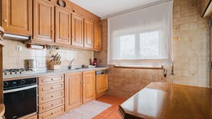 A kitchen with wooden cabinets, a built-in oven, a dishwasher, and a window with blinds. - Room 'Duplo Com Wc Privada' with Shared Garden and Wi-Fi (Apúlia)