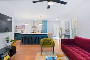 A modern living room with a red sofa, a green armchair, and a kitchen area with a blue island and bar stools.