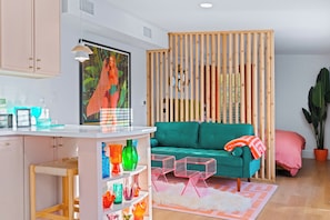A modern living room with a teal sofa, a wooden partition, and colorful glass vases on shelves.
