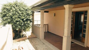 Un espace extérieur abrité, doté d’un sol en pierre, d’une rambarde en bois et d’un grand arbuste.