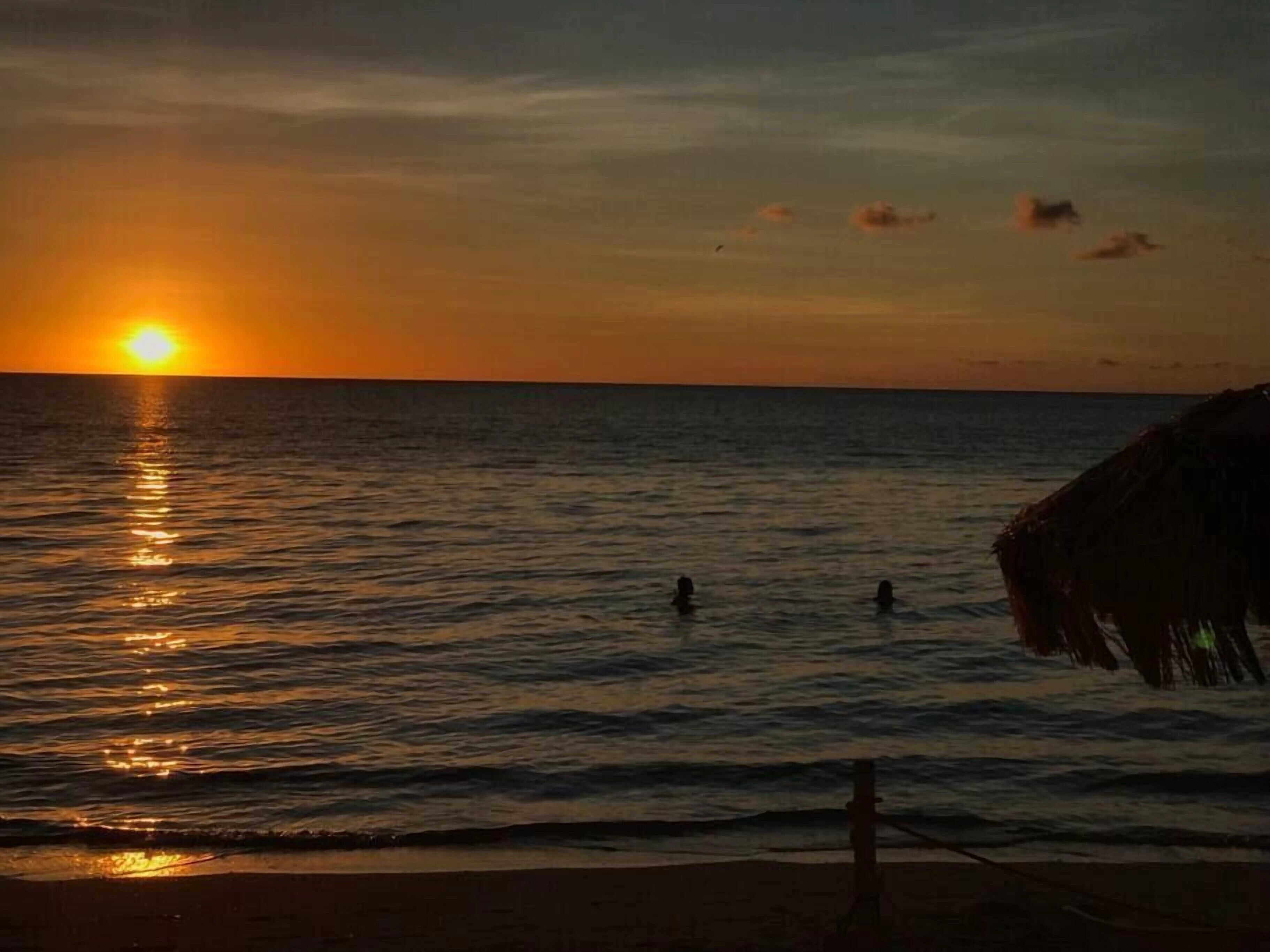 Un coucher de soleil sur l’océan, avec une plage et une construction à toit de chaume.