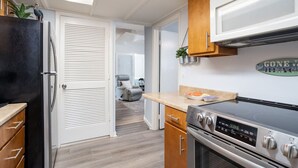 A compact kitchen with a refrigerator, stove, and wooden cabinets. - Cozy Cottage, 2 Queens, 1 Twin, Patio, Shared Pool (Melbourne)