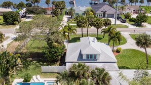 A residential area with a large house featuring a swimming pool, surrounded by palm trees and a view of the water. - Cozy Cottage, 2 Queens, 1 Twin, Patio, Shared Pool (Melbourne)