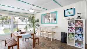 A room with a wooden table and chairs, a ceiling fan, a large window, and a shelf with folded towels. - Cozy Cottage, 2 Queens, 1 Twin, Patio, Shared Pool (Melbourne)