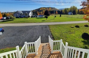 A residential driveway with a wooden staircase leading to a house, a clear sky, and a hilly landscape in the background.