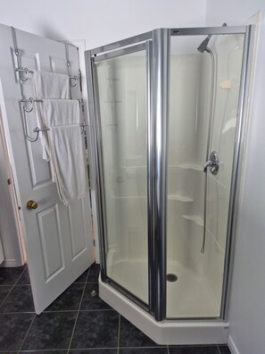 A glass-enclosed shower with a chrome frame, a white door with a towel rack, and dark tiled flooring.